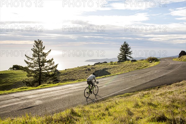 Caucasian man riding bicycle on road near ocean