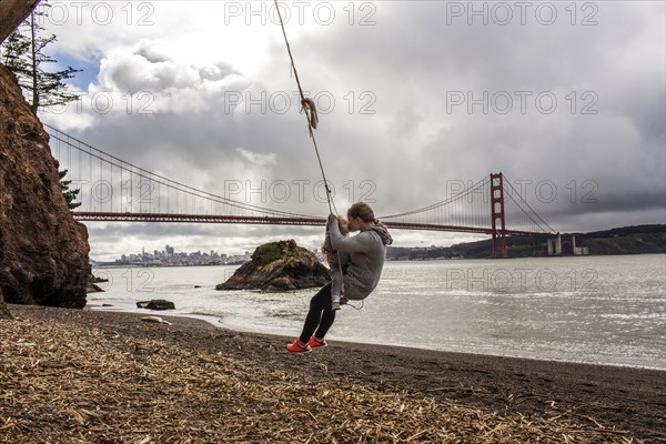 Caucasian mother and daughter on rope spring near bridge