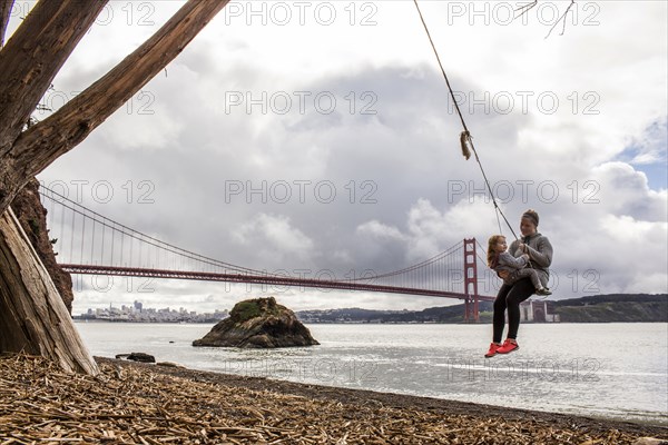 Caucasian mother and daughter on rope spring near bridge