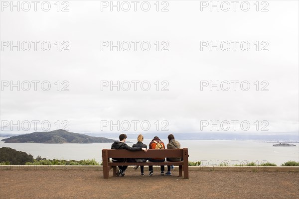 Friends sitting on bench admiring scenic view of ocean