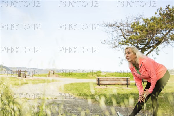Older Caucasian woman stretching leg in park