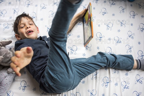 Playful Mixed Race boy laying on bed holding digital tablet