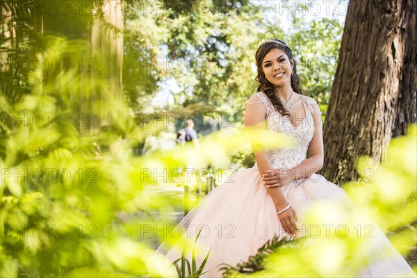 Portrait of a smiling Hispanic girl wearing gown near foliage