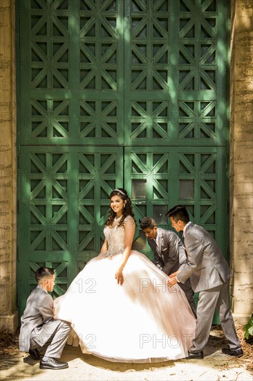 Hispanic boys wearing suits holding skirt of girl