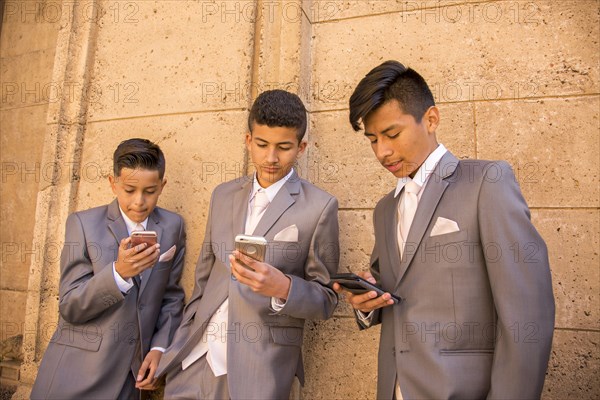 Hispanic boys wearing suits texting on cell phones