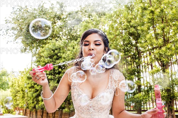 Hispanic girl wearing gown blowing bubbles