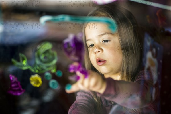 Mixed race girl finger painting on window