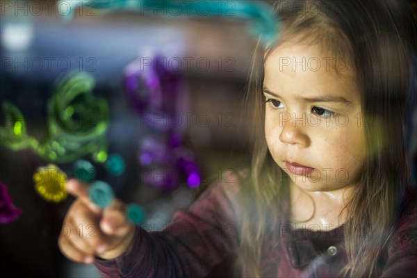 Mixed race girl finger painting on window