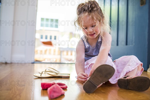 Caucasian girl sitting on floor fastening sandal