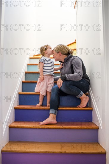 Caucasian girl kissing mother on forehead on multicolor staircase