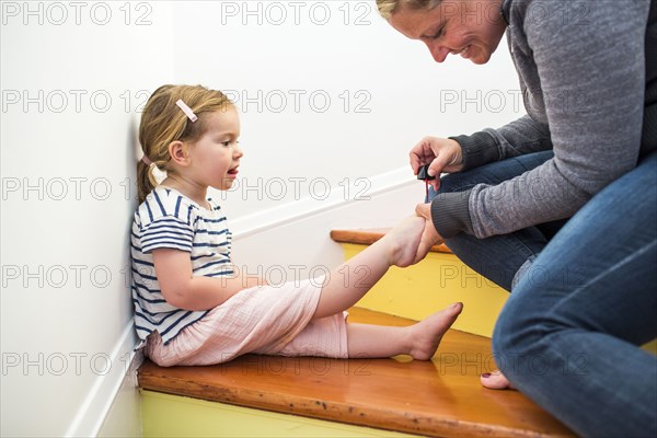 Caucasian mother painting toenails of daughter on staircase