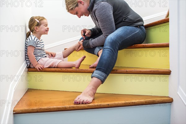 Caucasian mother painting toenails of daughter on multicolor staircase
