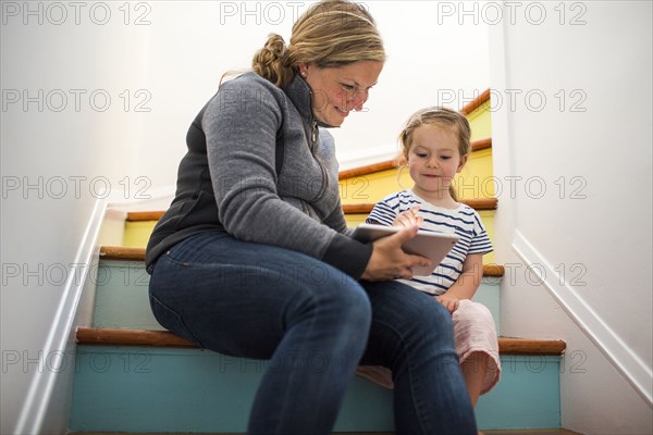 Caucasian mother and daughter using digital tablet on staircase