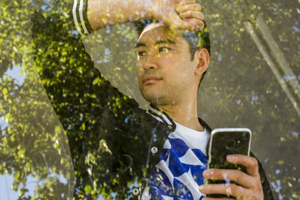 Serious Chinese man leaning on window holding cell phone