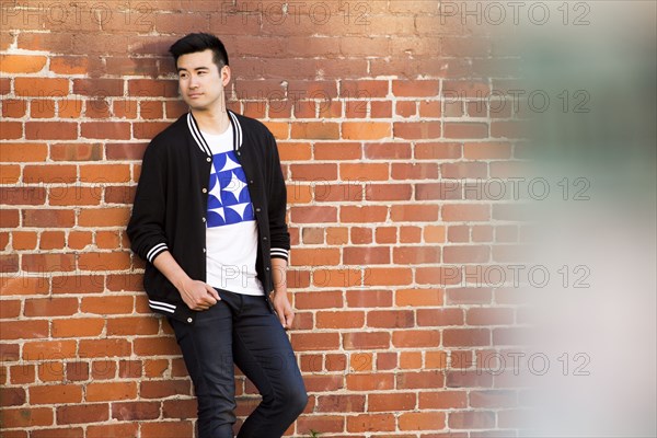 Smiling Chinese man leaning on red brick wall