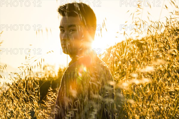 Serious Chinese man standing in field of wheat