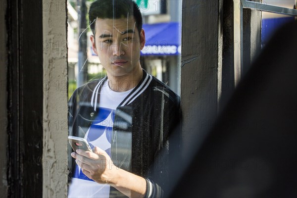 Serious Chinese man texting on cell phone behind window