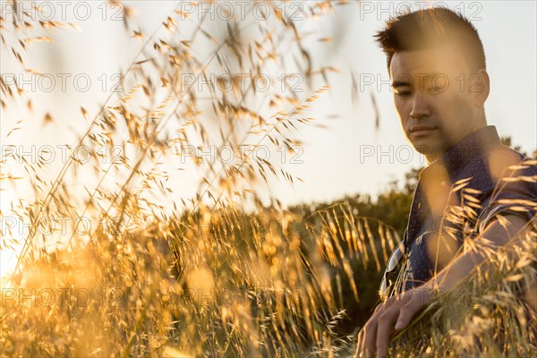 Serious Chinese man sitting in field of wheat