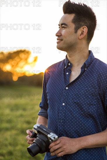 Smiling Chinese man holding camera in field