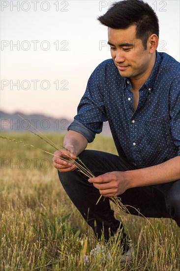 Smiling Chinese man crouching and holding grass in field