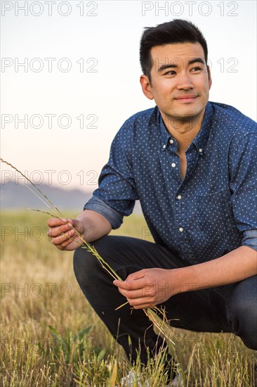 Smiling Chinese man crouching and holding grass in field