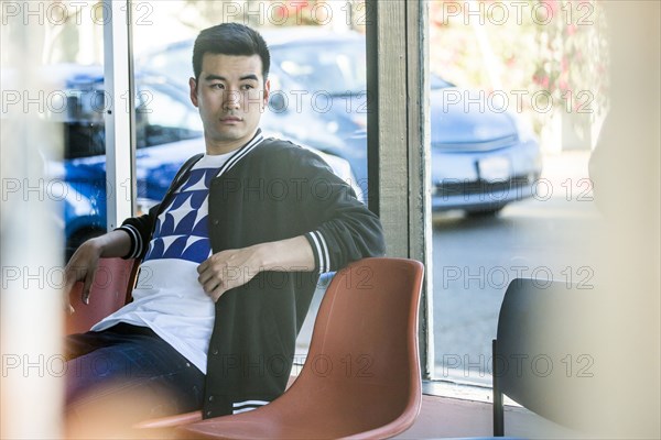 Serious Chinese man sitting in chair near window