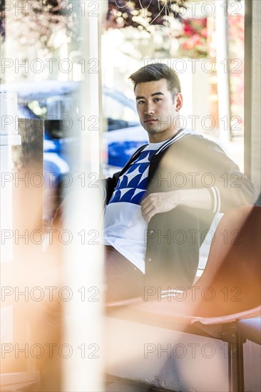 Serious Chinese man sitting in chair near window