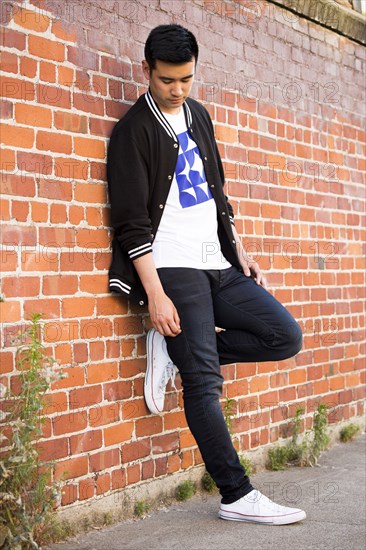 Pensive Chinese man leaning on brick wall