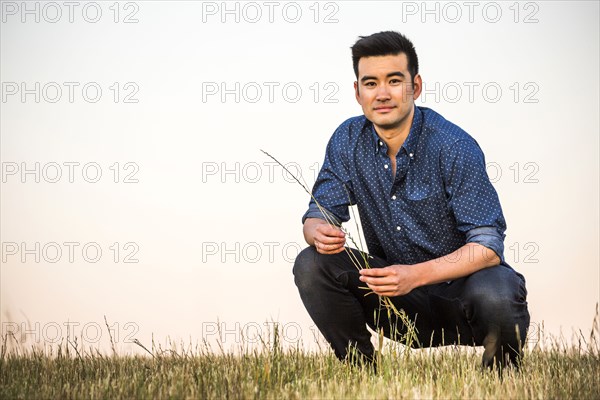 Chinese man crouching in field holding grass