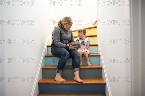 Caucasian mother and daughter using digital tablet on staircase