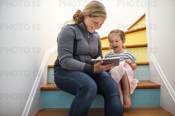 Caucasian mother and daughter using digital tablet on staircase