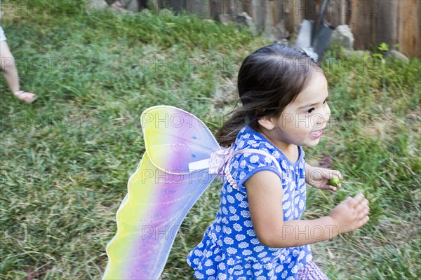 Mixed race girl running wearing fairy wings