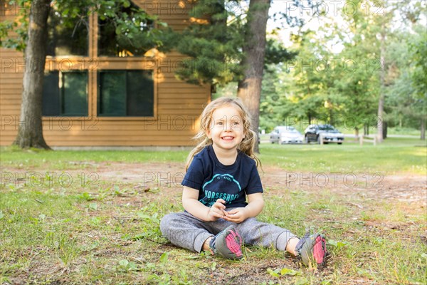 Smiling Caucasian girl sitting on ground outside house