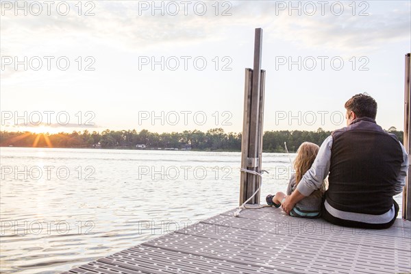 Caucasian father and daughter sitting on pier at sunset
