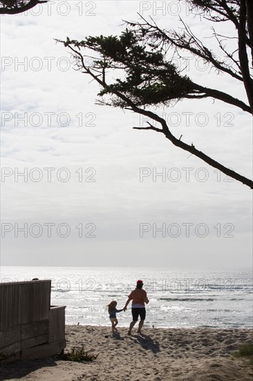 Caucasian mother and daughter holding hands and running on beach
