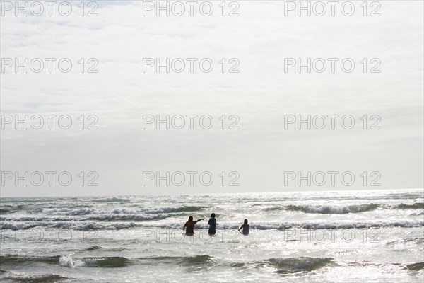 Caucasian people wading in ocean waves