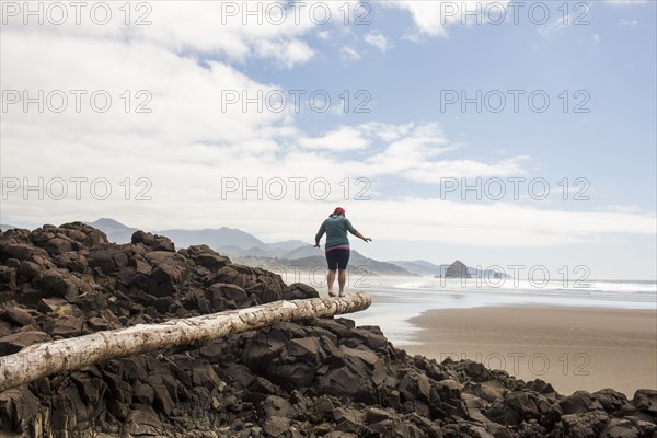 Caucasian woman balancing on log on rocks at beach