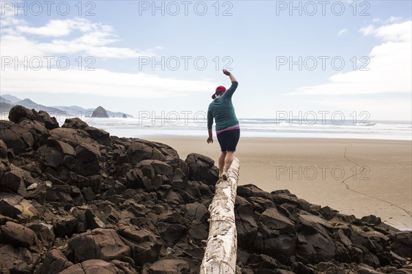 Caucasian woman balancing on log on rocks at beach