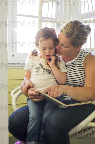 Caucasian mother reading book to daughter on lap