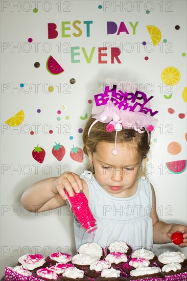 Caucasian girl sprinkling sprinkles on tray of cupcakes for birthday