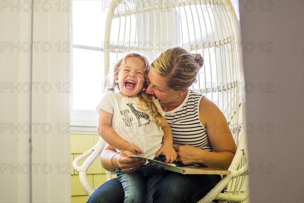 Playful Caucasian mother biting shoulder of daughter reading book