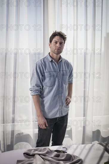 Caucasian man standing near curtains in bedroom