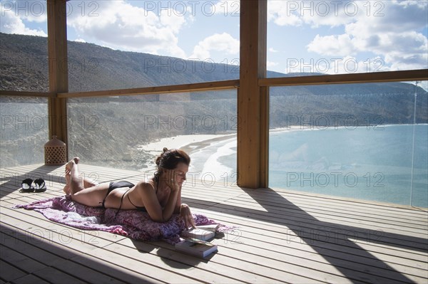 Caucasian woman sunbathing on deck over beach