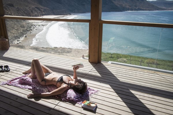 Caucasian woman sunbathing and reading book on deck over beach