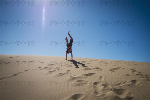 Caucasian teenage boy doing cartwheels on sand dune