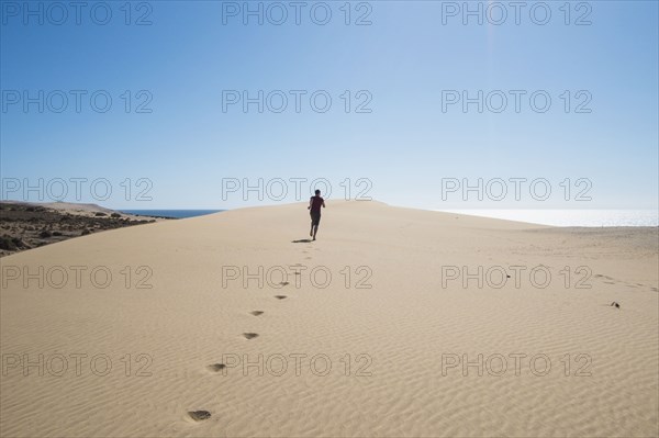 Caucasian teenage boy running on sand dune