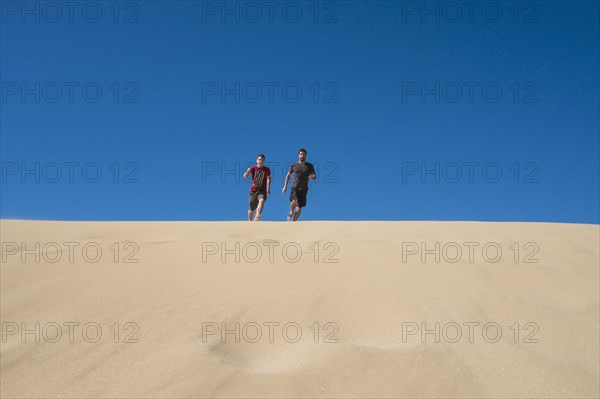 Caucasian father and son running on sand dune