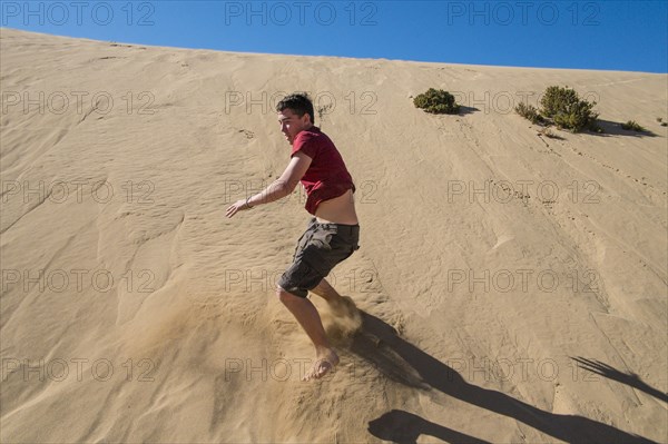Caucasian teenage boy sliding on sand dune