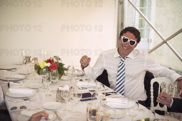Caucasian man wearing heart-shaped glasses at table