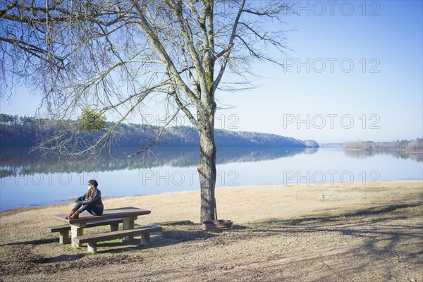 Caucasian woman sitting on bench near rural river